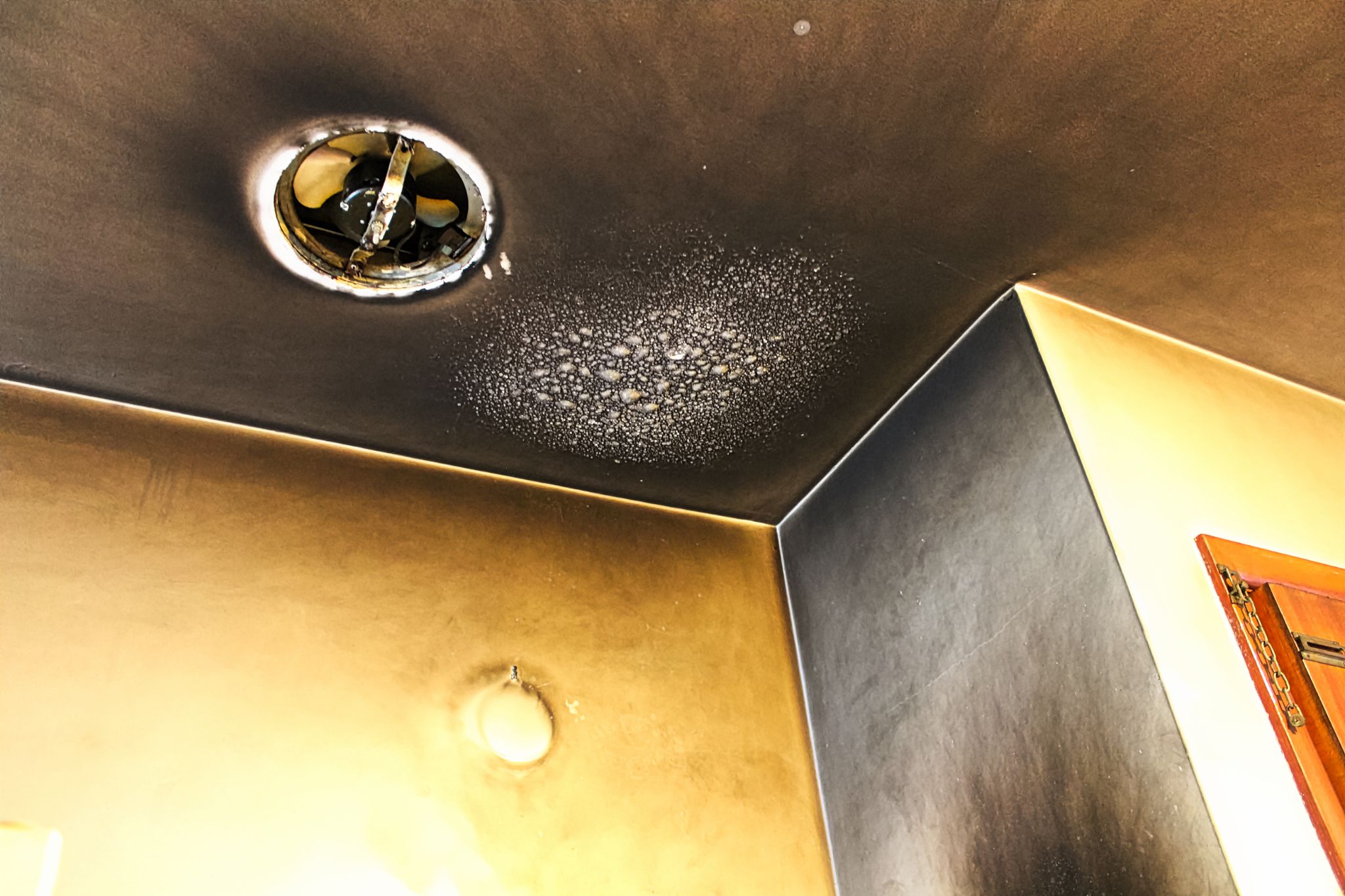 Severe soot accumulation and fire damage on ceiling and walls around an exhaust fan.