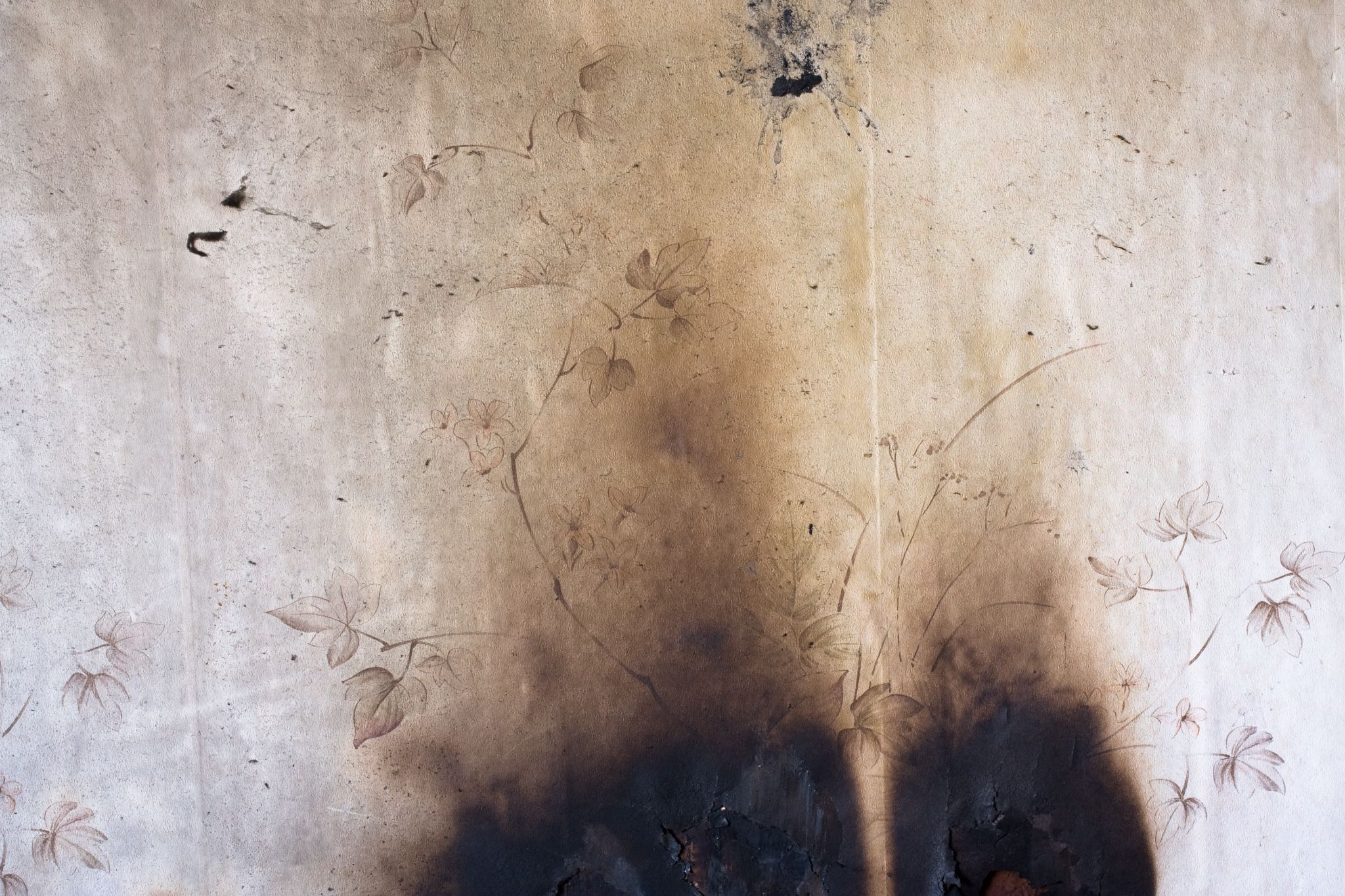 Soot marks and scorch damage on floral wallpaper from fire exposure.