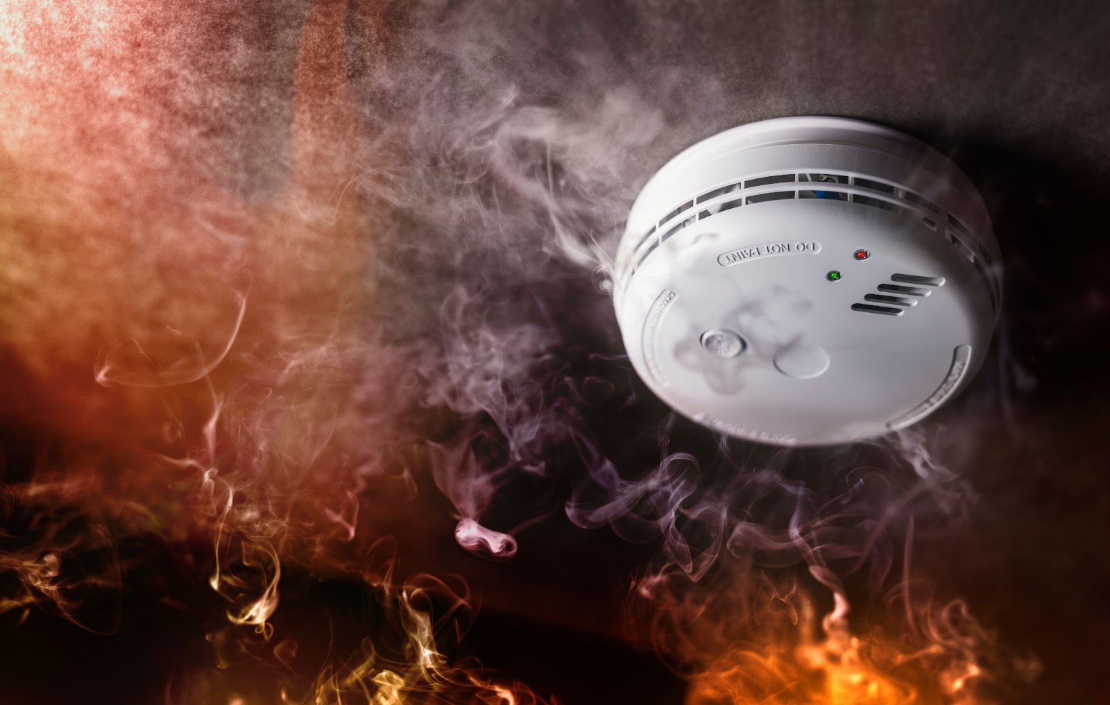 Smoke detector surrounded by flames, emphasizing importance of fire prevention and suppression systems