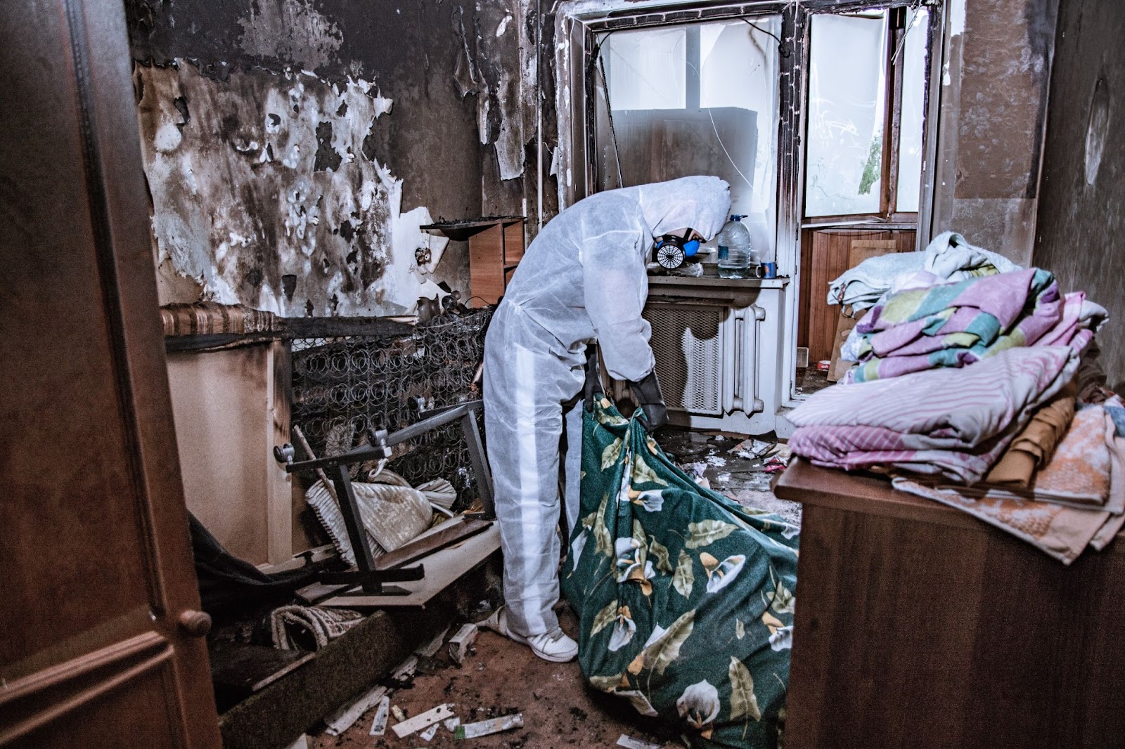 A person in a white protective suit stands in a room with a bed and other items, after a house fire for fire restoration