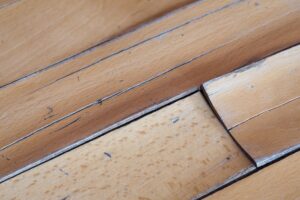 Close-up of warped and peeling light wood floor planks showing water damage.