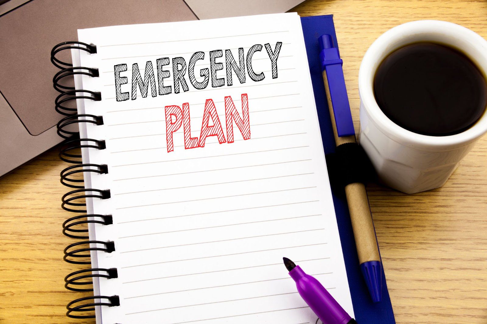 Notebook with emergency plan, coffee, and pen. Keywords natural disasters, disaster preparedness, emergency situation.