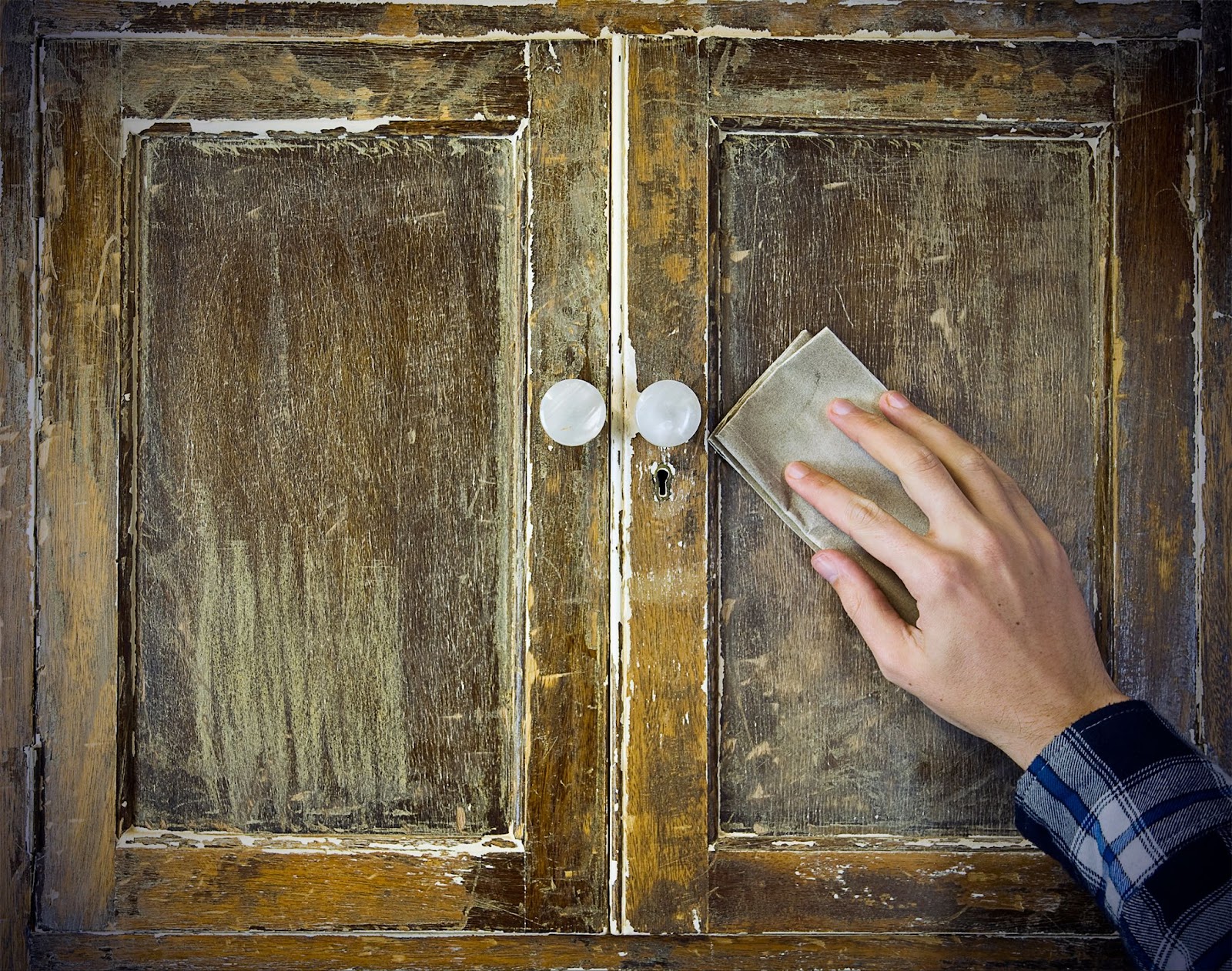 A person cleans a wooden cabinet with a sponge, addressing water damage and restoring its original condition.