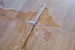 Close-up of a wood floor showing water accumulation, highlighting the effects of water damage on wooden surfaces.