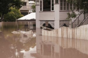 Flooded residential area with a house and fence, highlighting the impact of water damage and the restoration process needed.