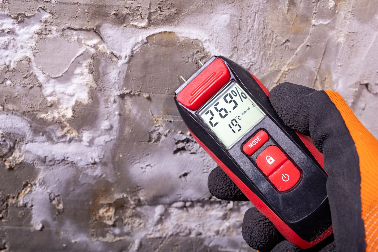 A person checks a digital thermometer against a wall, highlighting mold damage restoration efforts in a bathroom setting.