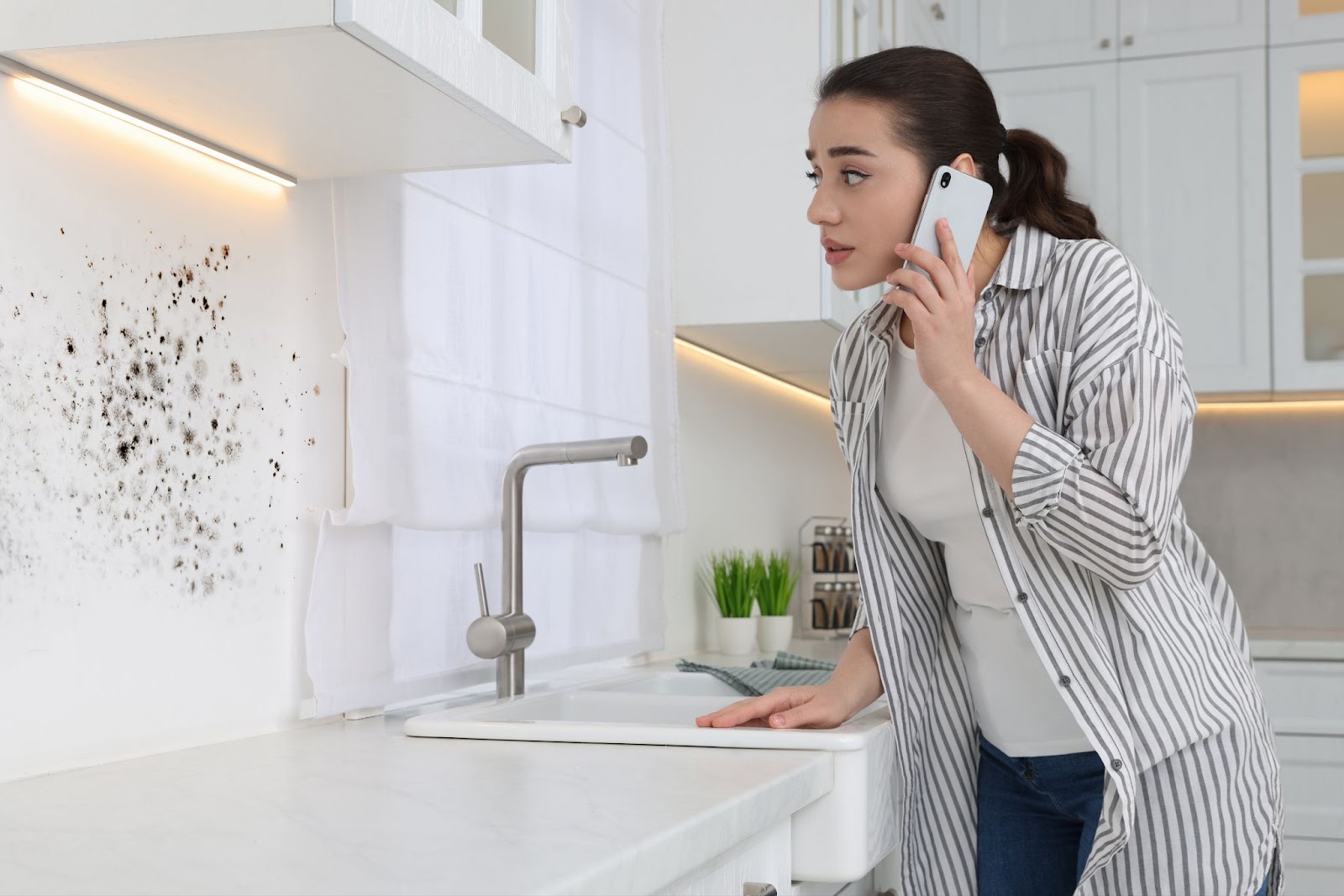 A woman converses on a cell phone in a kitchen, emphasizing the importance of professional mold remediation services.