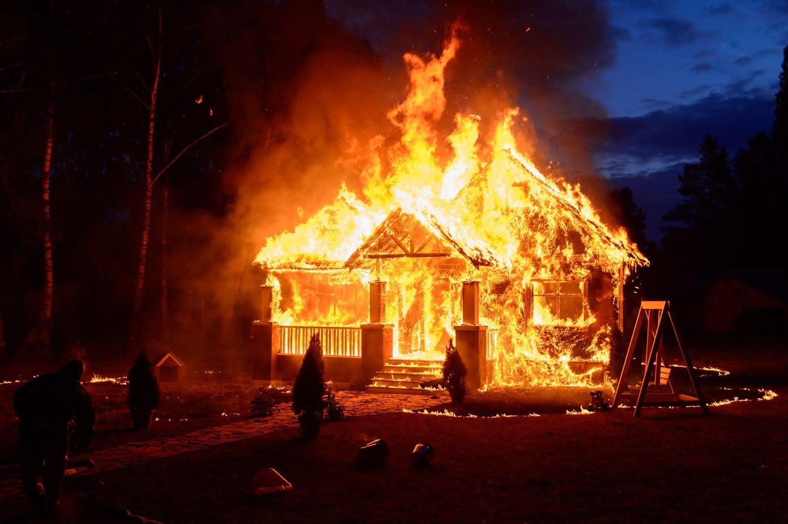 A burning house surrounded by onlookers who appear concerned about the fire