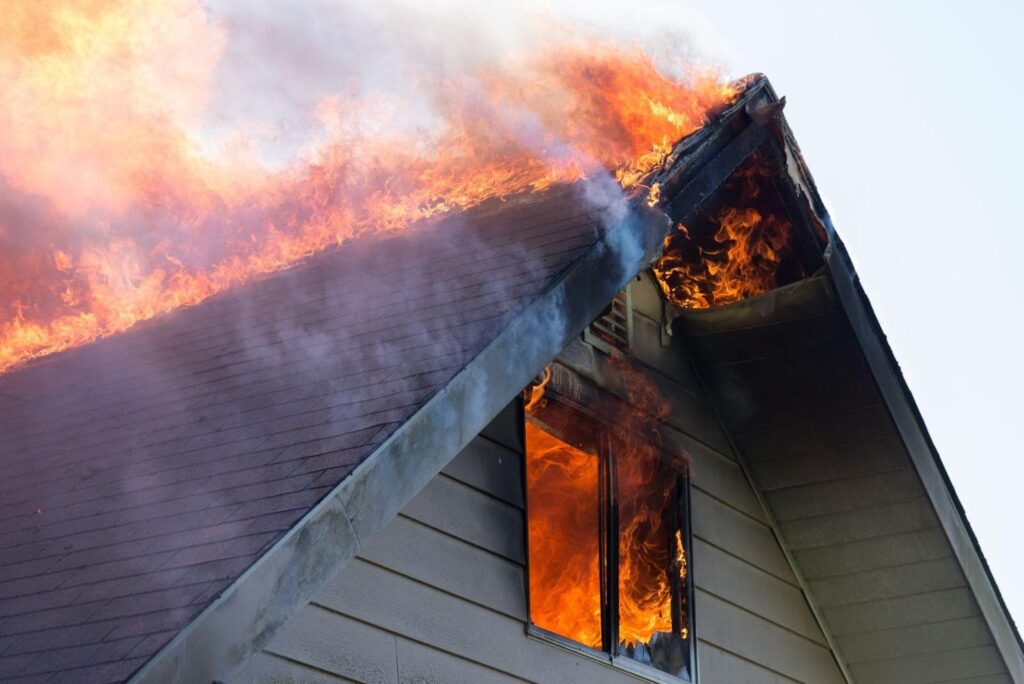 A house with flames erupting from the roof indicating a fire emergency in progress