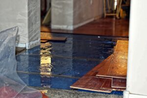 Wet construction site with wooden planks and plastic covering on a tiled floor.
