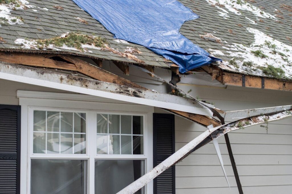 A blue tarp covers a damaged roof highlighting urgent repair needs after bad weather