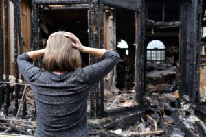 A woman stands solemnly in front of a charred house reflecting on the aftermath of a fire