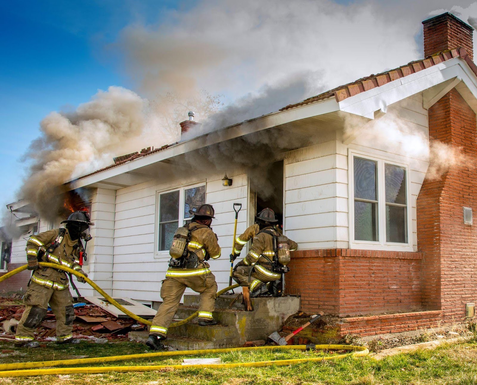 Firefighters extinguishing flames from a house fire in the front yard with smoke billowing into the sky