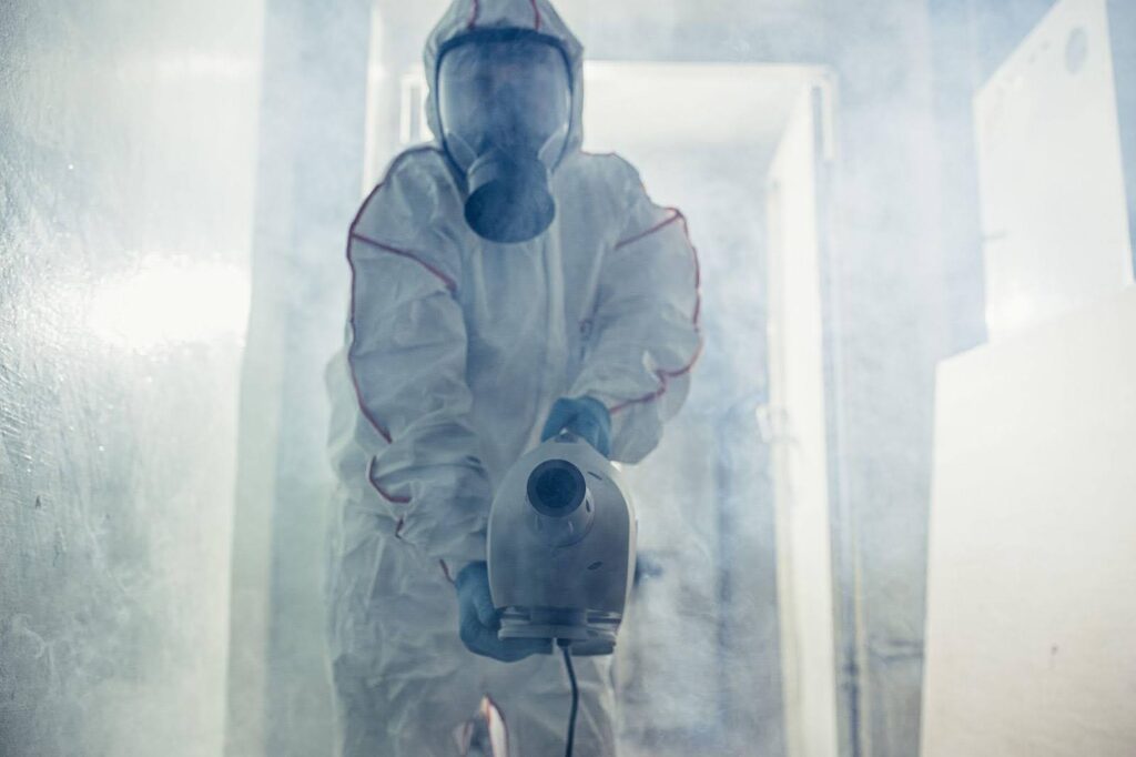 A person in a protective suit sprays disinfectant in a room ensuring a sanitized environment