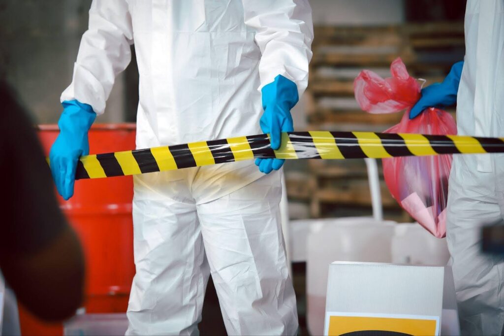 A person in a white suit and blue gloves holds yellow and black tape for measurement