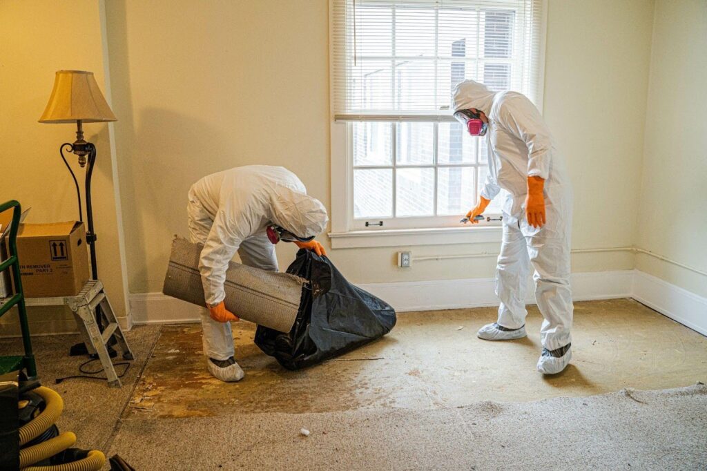 Two men in protective gear and masks are thoroughly cleaning a room to ensure a safe environment