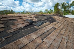 Damaged roof shingles showing signs of wind damage, with several shingles lifted and missing.