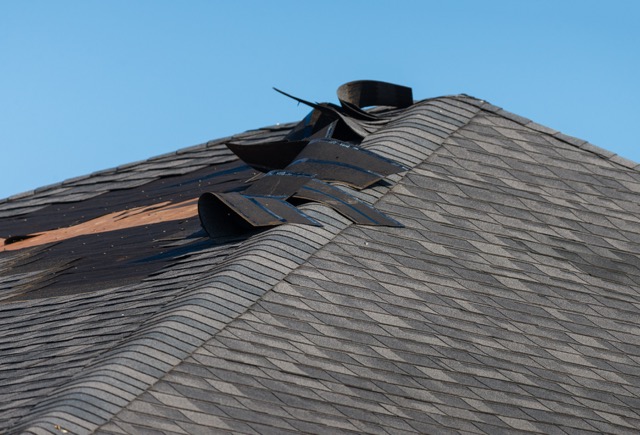 Roof with damaged shingles and a broken window, showing signs of wind damage.