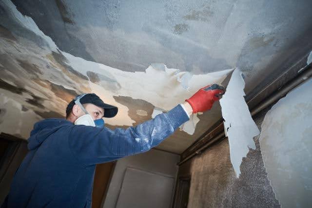 A man wearing a blue shirt and red hat is painting the ceiling with a roller