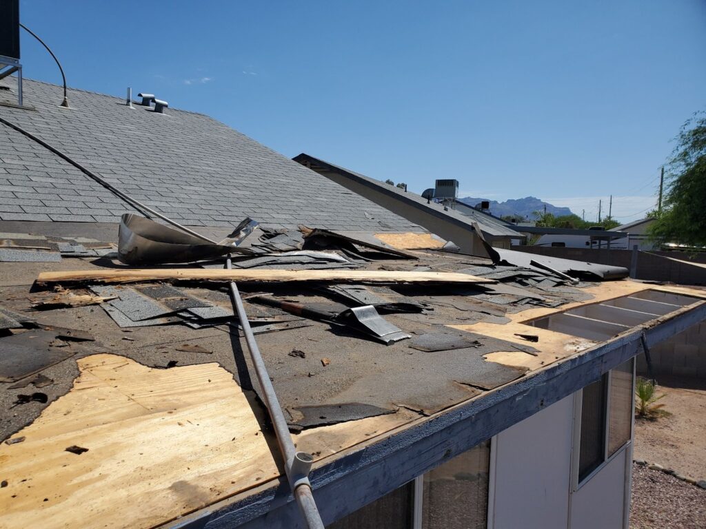 A damaged house roof with torn shingles and exposed plywood underlayment undergoing repairs.