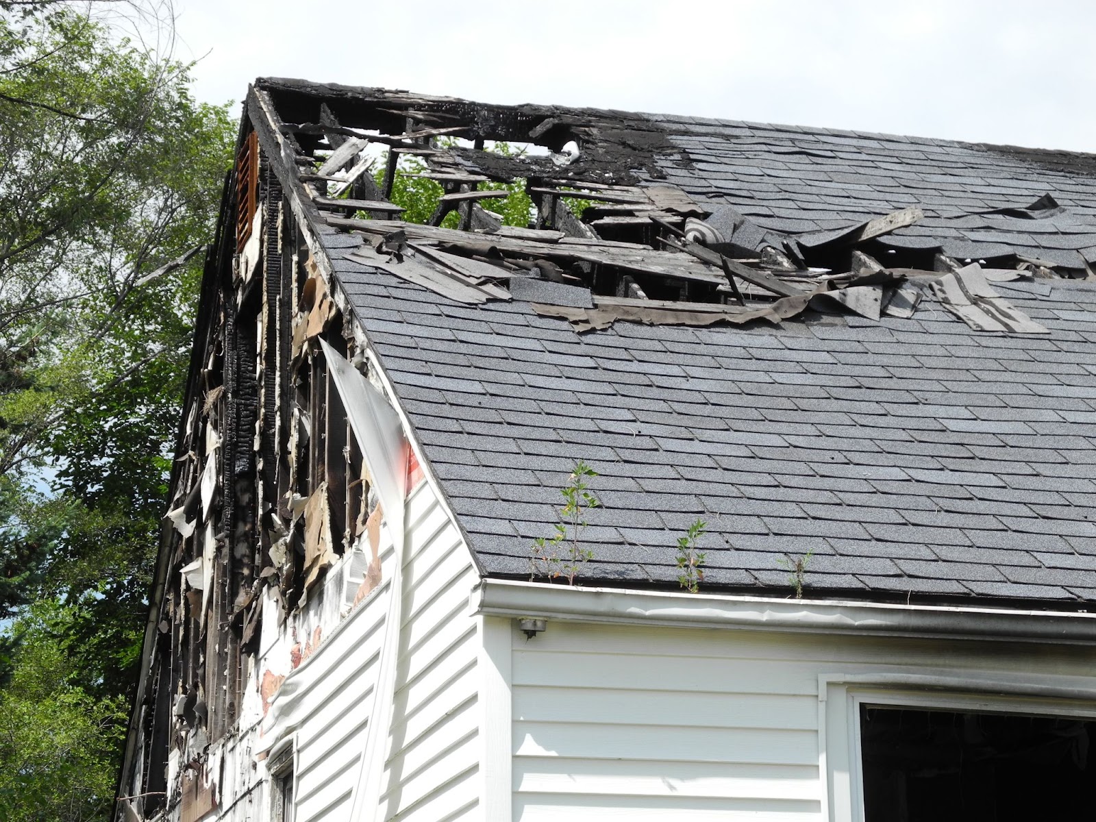 A close-up view of a house roof featuring a large hole and extensive charring from fire damage.
