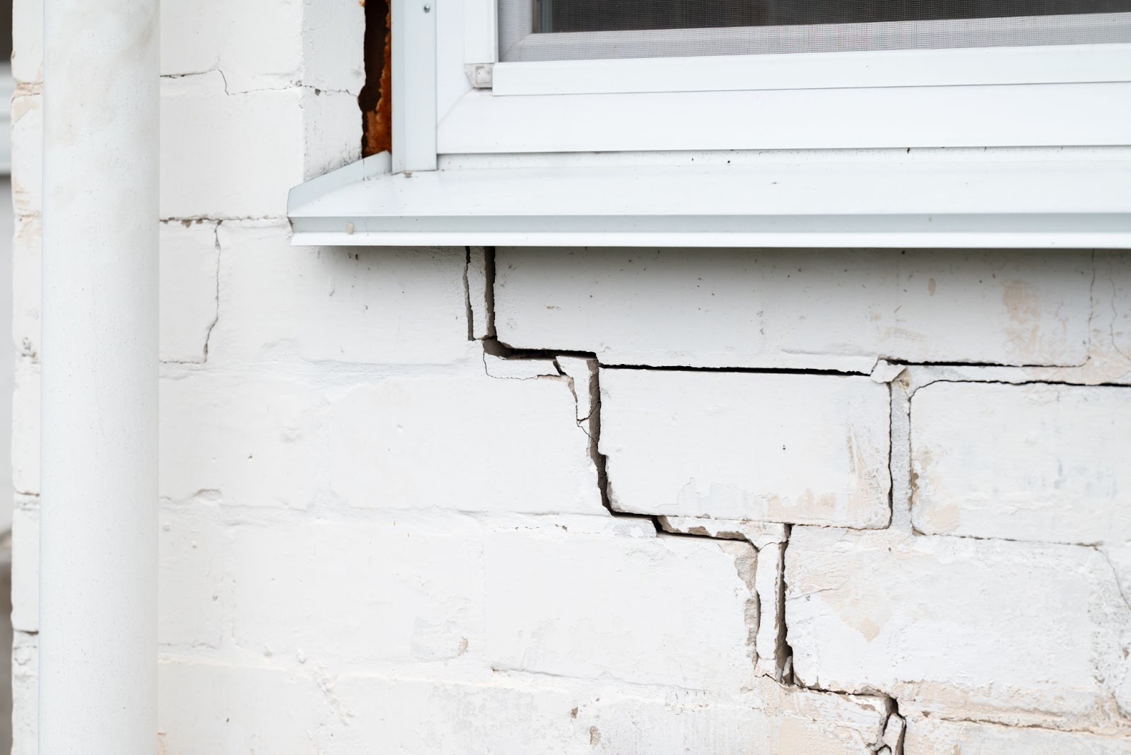 A stair-step crack spreads across a white brick wall beneath an exterior window sill.