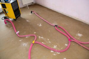 Interior view of a room with pink hoses scattered around and a yellow machine prominently displayed