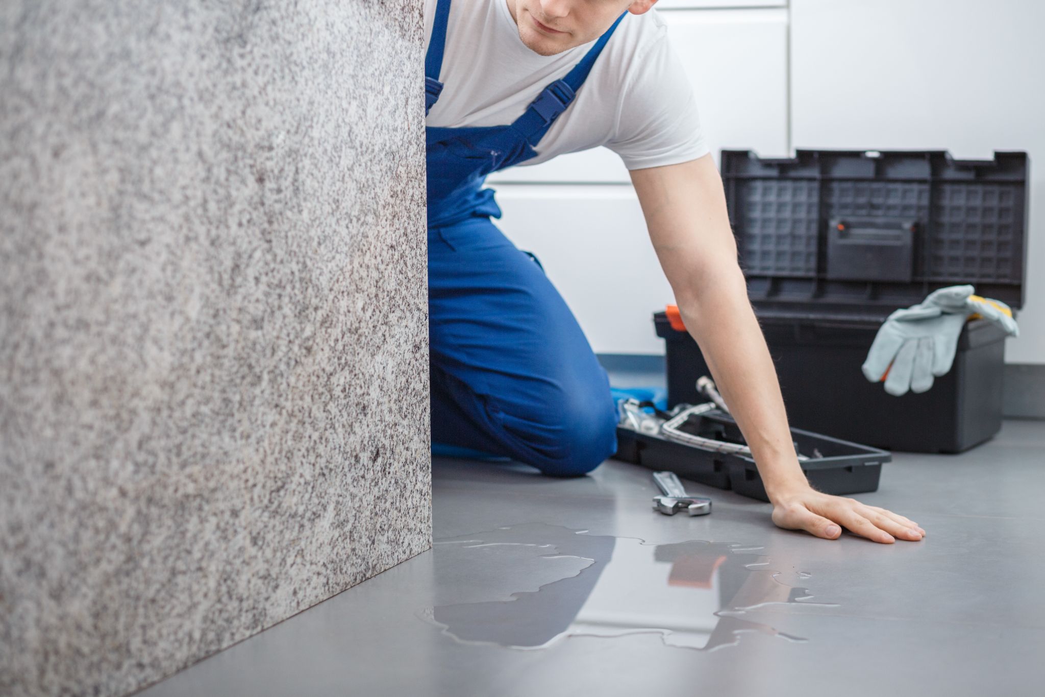 A plumber checking a water leak on the floor next to his toolbox.