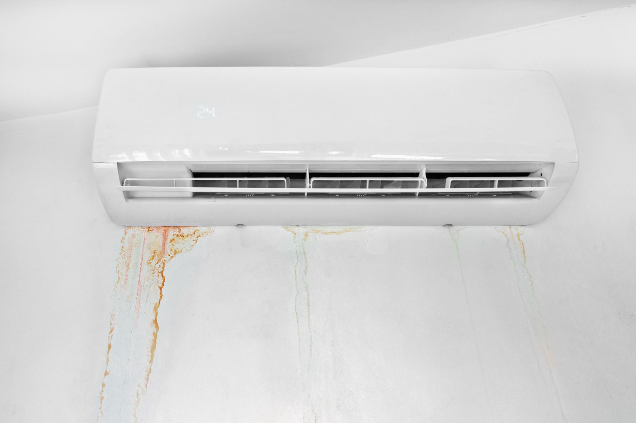 A white air conditioner unit leaking and causing brown water stains on a white wall.