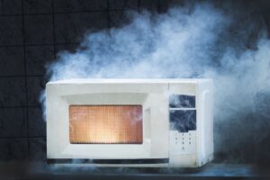 A white microwave oven emitting thick smoke with a glowing orange light inside its window.