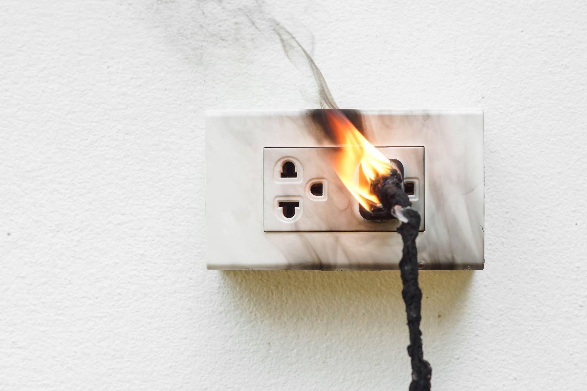 An electric outlet with a plug emitting smoke and flames indicating a potential fire hazard