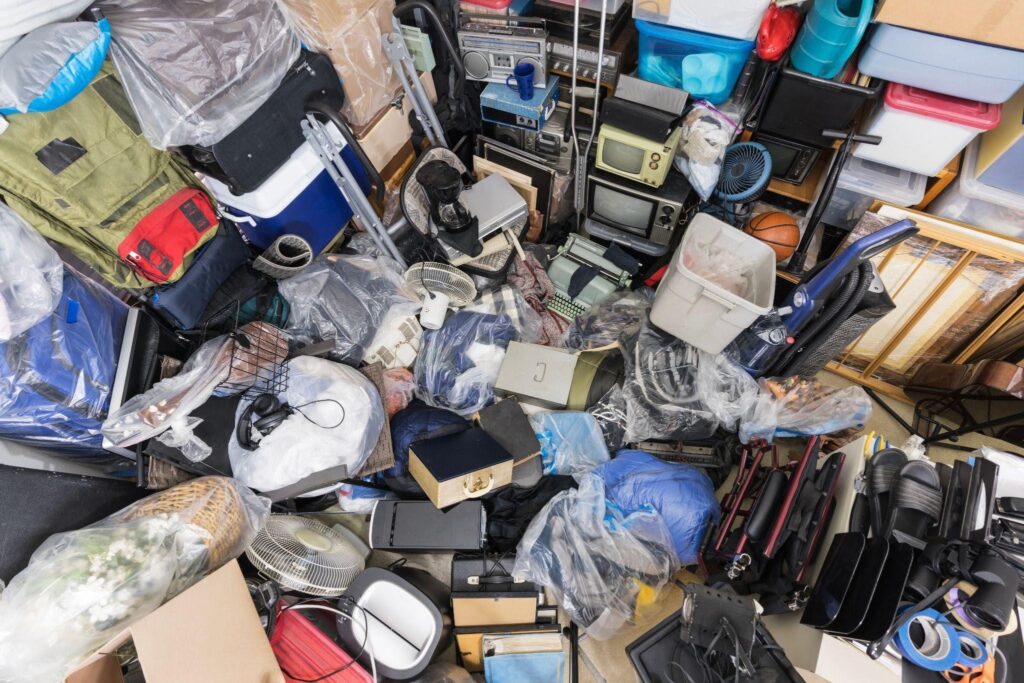 A chaotic pile of secondhand goods including electronics bags sports gear containers tools and household items