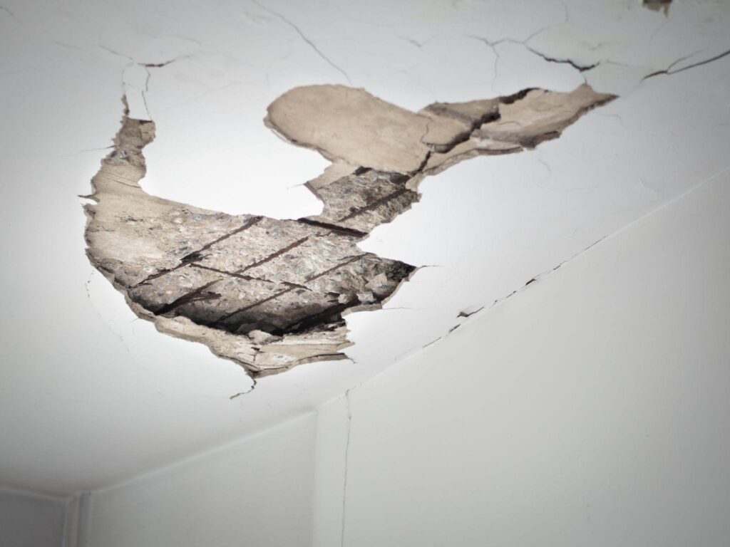 A damaged ceiling featuring a noticeable hole revealing structural issues above