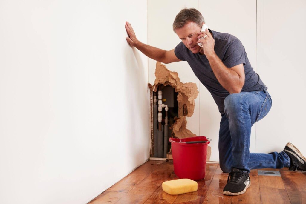 A man kneels on the floor beside a red bucket preparing to clean or organize the area