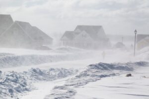 Suburban neighborhood street during a heavy winter blizzard with thick snowbanks and blowing snow.